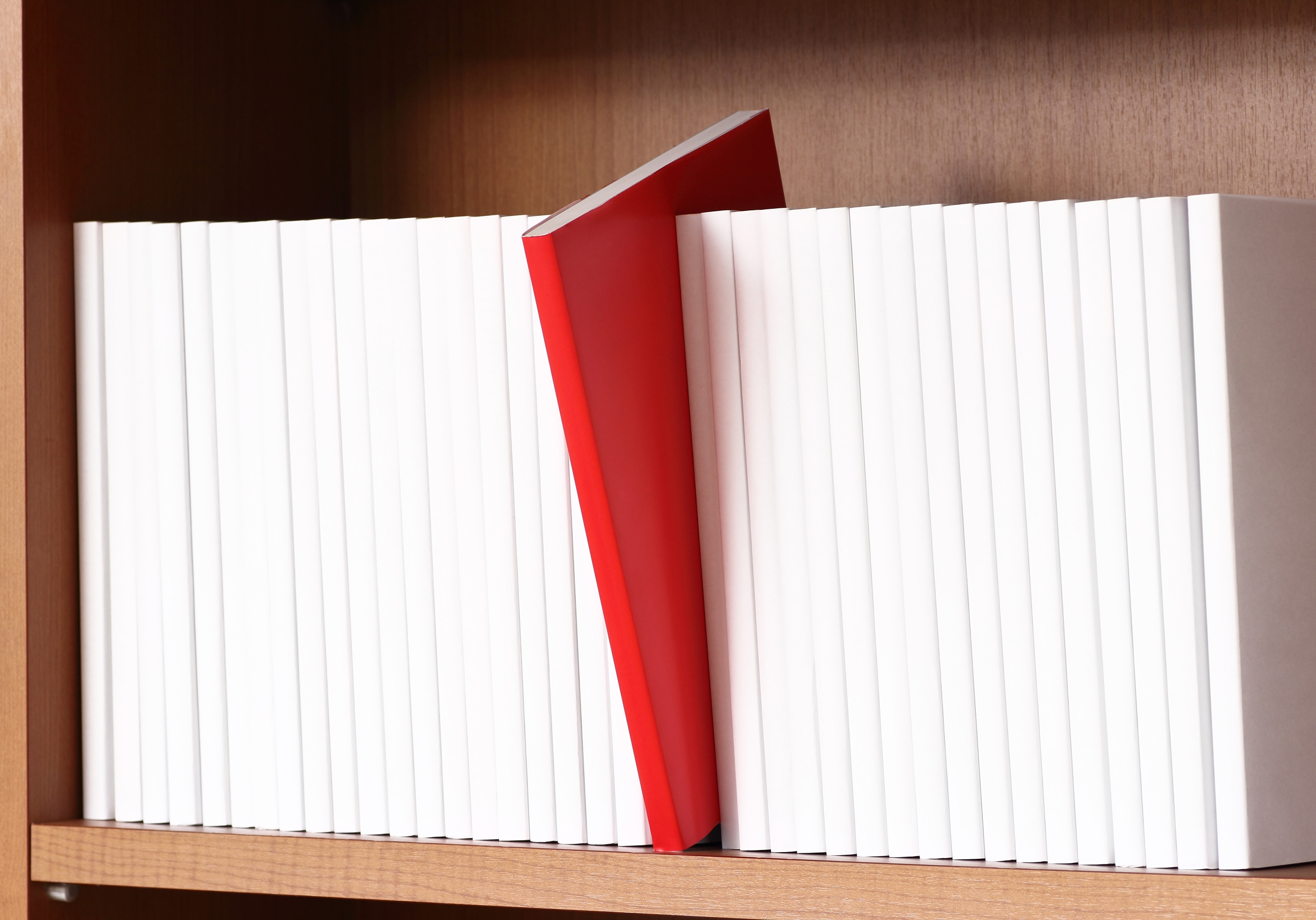 棚に並べられた白い本と、その中に差し込まれた1冊の赤い本のクローズアップ。