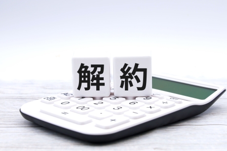 電卓の上に「解約」と書かれた2つの白いブロックが置かれている。これは、契約の解除、費用計算、または金融取引における解約の概念を示唆している。