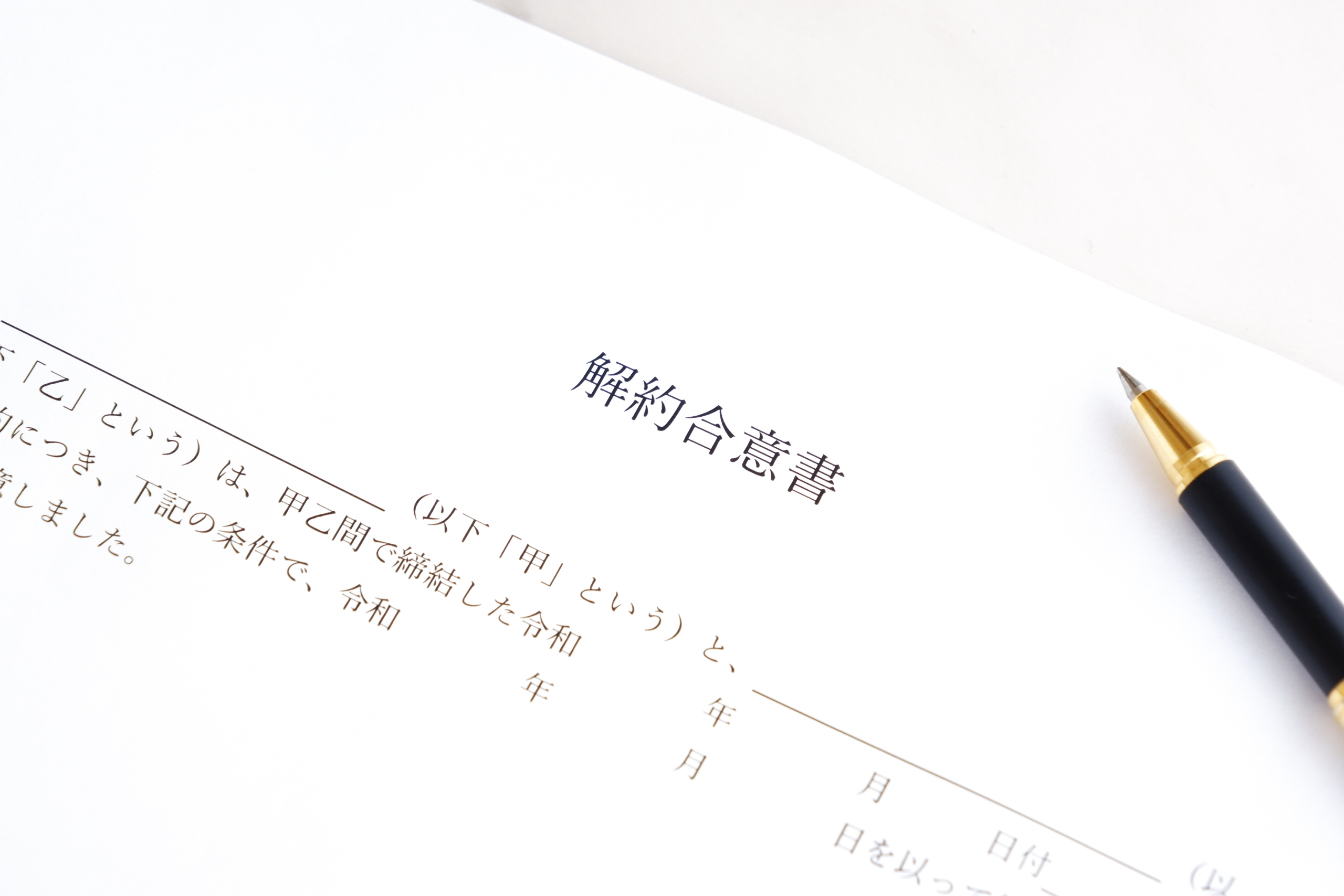 白い書類に「解約合意書」とタイトルがあり、その右横に黒と金のペンが置かれている。これは、契約の解除、終了、または合意書の署名を示唆している。