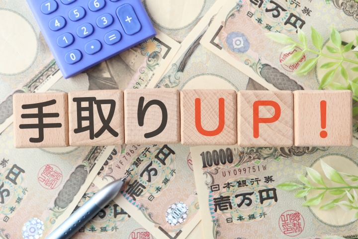 一万円札の上に「手取りUP！」の文字が書かれた積み木が置かれ、電卓やペンが添えられた、手取り額増加や収入アップのイメージ画像