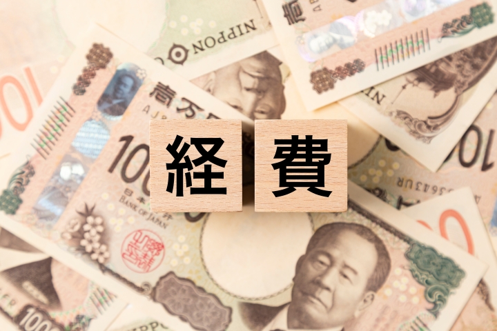 日本の一万円札の上に置かれた「経費」と書かれた木製ブロック。経理、会計、支出管理のイメージ