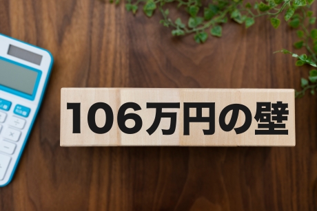 「106万円の壁」と書かれた木製ブロックと電卓が置かれた机の上