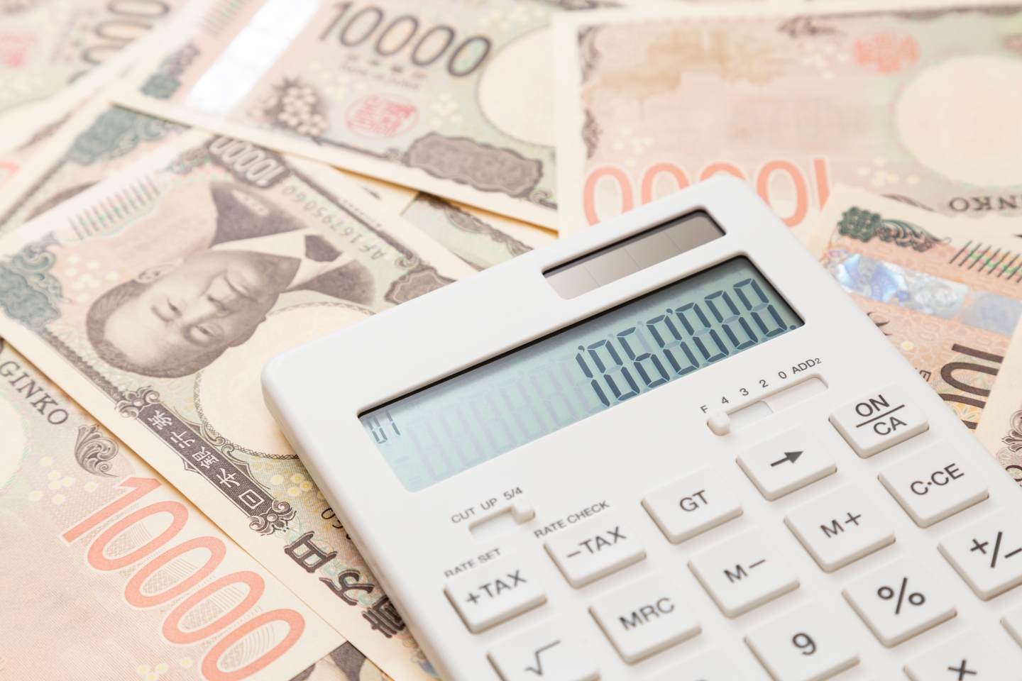 液晶画面に「1060000」と表示された白い電卓と、背景に広がる1万円札