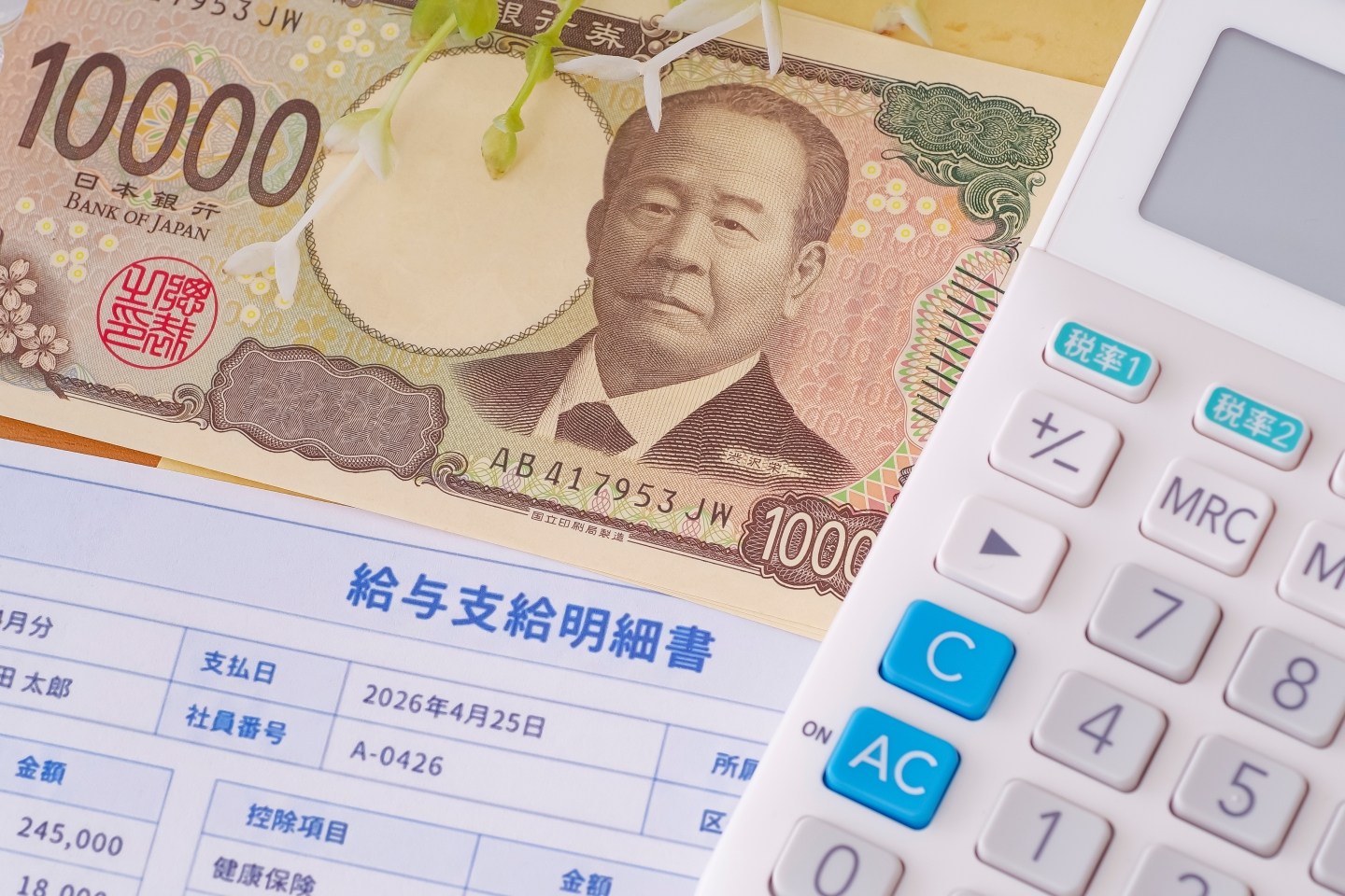 給与支給明細書と新1万円札、電卓が並べられた様子