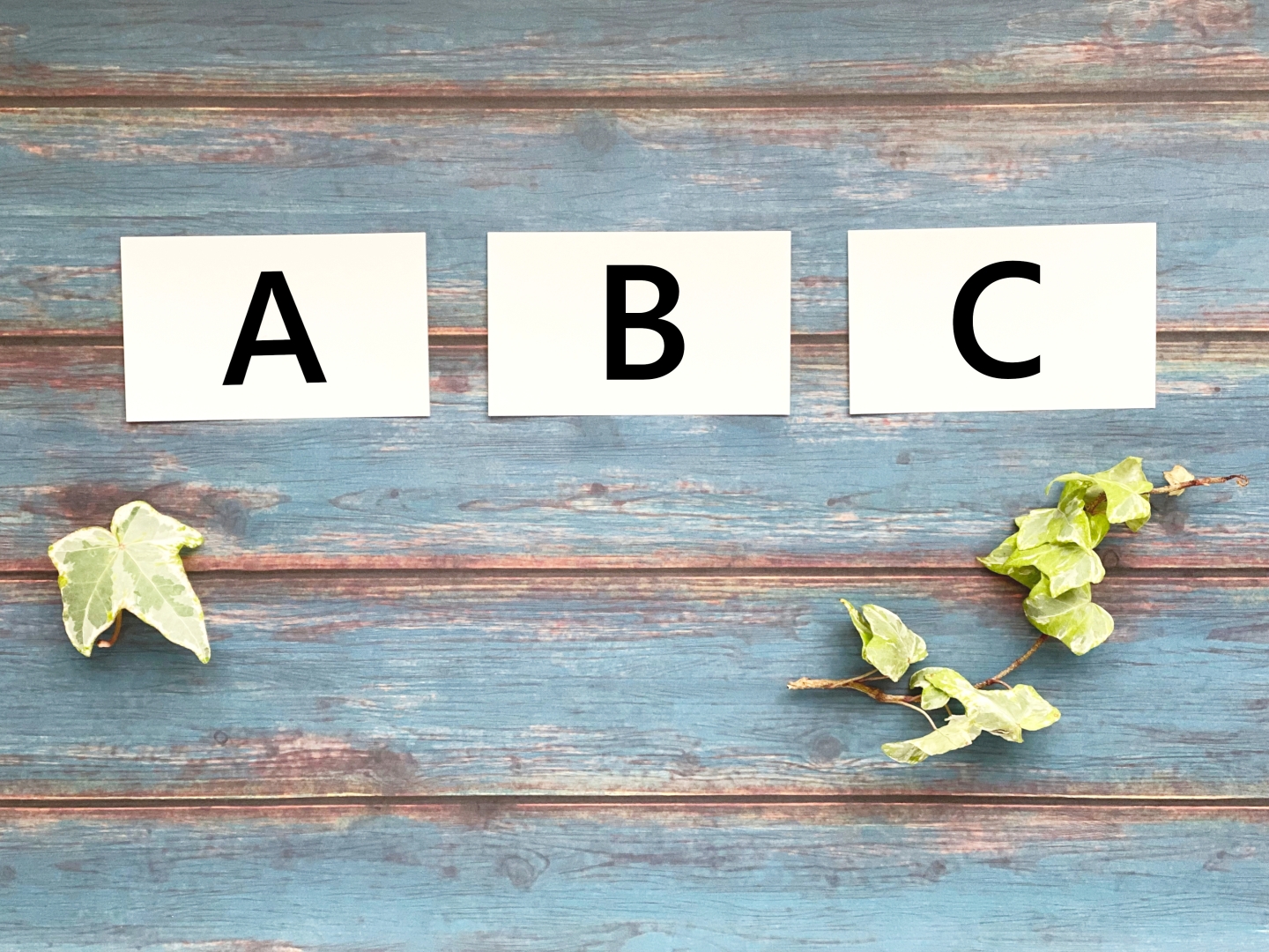 「A」「B」「C」と書かれたカードとアイビーの葉が飾られた木目調の背景